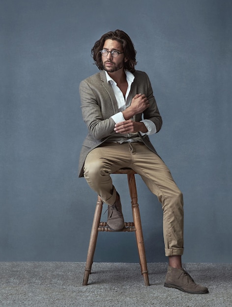 Hes got style Prise de vue en studio pleine longueur d'un beau et élégant jeune homme assis sur un tabouret sur un fond gris