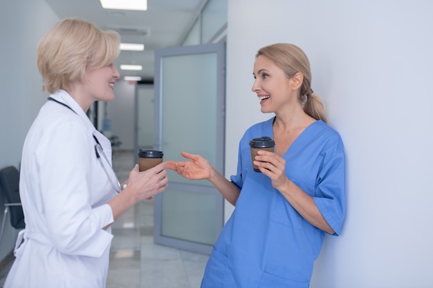 L'heure du café. Deux femmes médecins souriant debout dans le couloir, boire du café