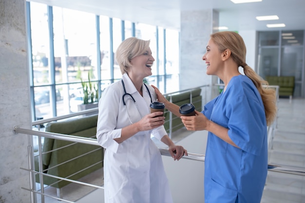 L'heure du café. Deux travailleuses médicales souriantes s'appuyant sur la rampe d'escalier, boire du café