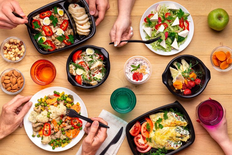 Photo heure du déjeuner saine sur le lieu de travail du bureau. quatre personnes mangeant des repas sains dans des boîtes à lunch et des assiettes à emporter sur une table en bois. concept, vue de dessus