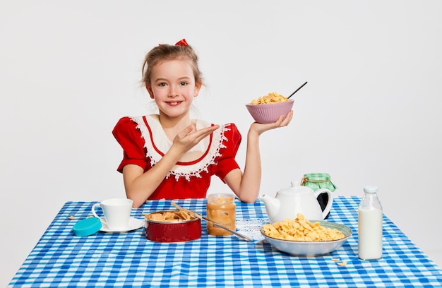 L'heure du petit déjeuner Portrait de belle petite fille enfant posant à table à manger avec des céréales sur fond de studio gris Concept de l'enfance