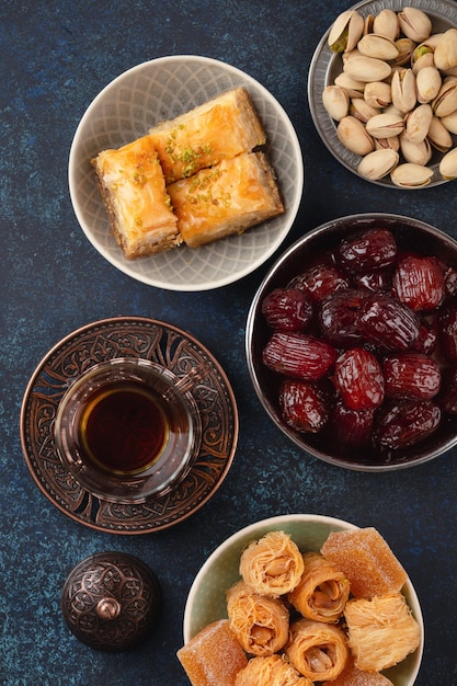 L'heure du thé chaud frais arabe traditionnel avec des bonbons, du baklava, des dattes, du lokum d'en haut. Snack du Ramadan avec délices turcs et pâtisserie arabe sur fond bleu rustique vue de dessus