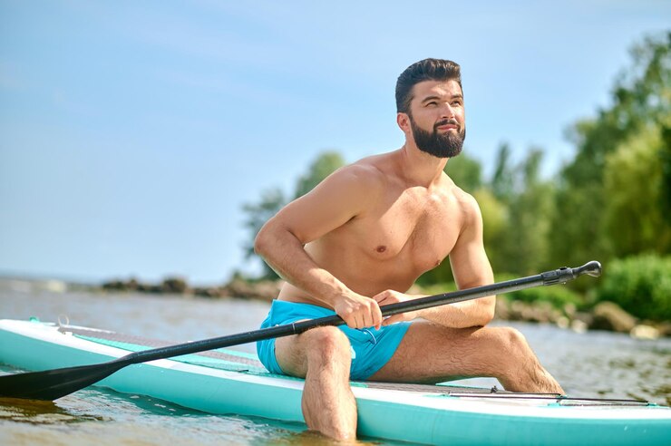 Photo heure d'été. jeune homme bien bâti en short bleu kayak