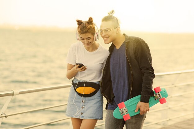 L'heure d'été de la jeunesse. Couple hipster élégant amoureux se promener le long de la promenade de la plage et écouter de la musique avec des écouteurs.