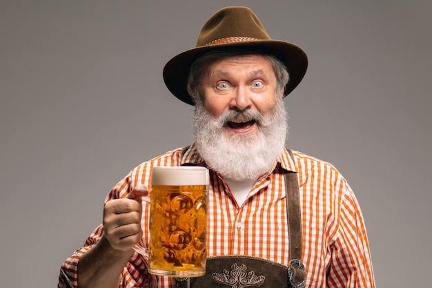 L'heure de la fête. Happy senior man habillé en costume traditionnel autrichien ou bavarois avec chope de bière sur fond gris studio. Espace de copie. La célébration, l'oktoberfest, le festival, le concept de traditions.