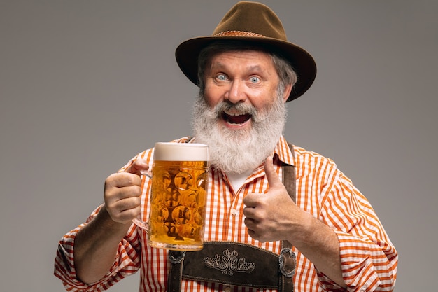 L'heure de la fête. Happy senior man habillé en costume traditionnel autrichien ou bavarois avec chope de bière sur fond gris studio. Espace de copie. La célébration, l'oktoberfest, le festival, le concept de traditions.