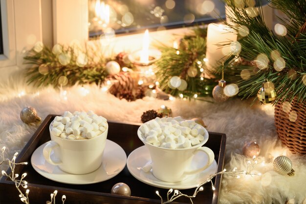 Heure d'hiver confortable avec des bougies de guimauve de café de Noël et une guirlande sur le rebord de la fenêtre