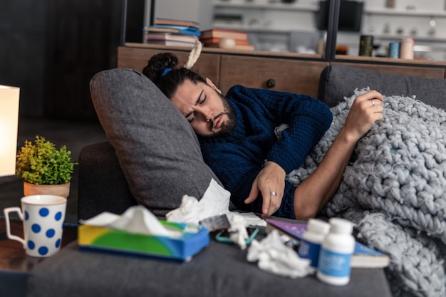 L'heure de la médecine. Triste homme malade voulant prendre ses pilules en position allongée sur le canapé