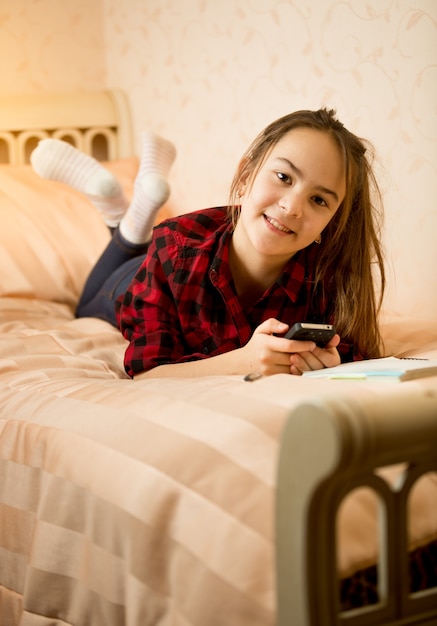 Heureuse adolescente allongée sur le lit et en tapant un message