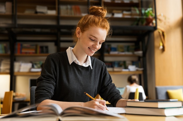 Heureuse adolescente aux cheveux rouges étudie à la table