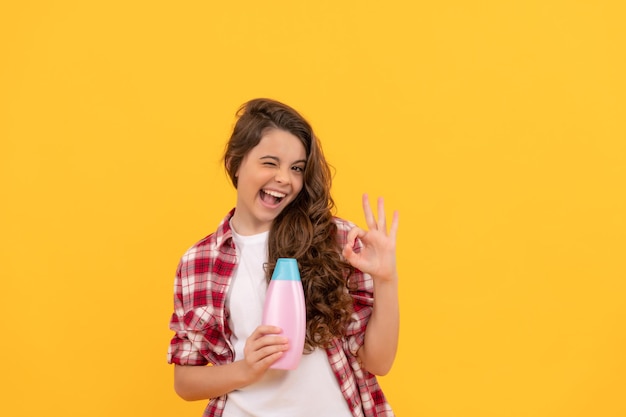 Heureuse adolescente aux longs cheveux bouclés tenir une annonce de bouteille de shampoing