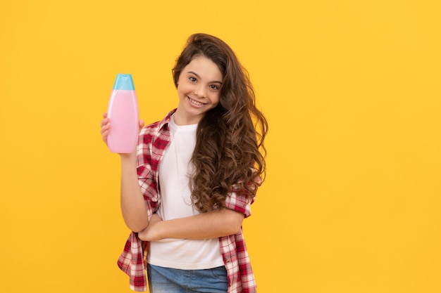 Heureuse adolescente aux longs cheveux bouclés tenir une bouteille de shampoing soins capillaires