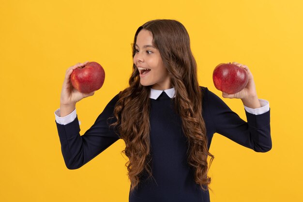 Heureuse adolescente choisissant une pomme vitaminée rouge pour le déjeuner sur fond jaune, choix.