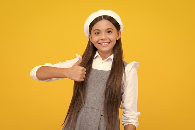 Heureuse adolescente décontractée enfant fille montrant le pouce vers le haut et souriant isolé sur fond jaune Bonne fille face à des émotions positives et souriantes