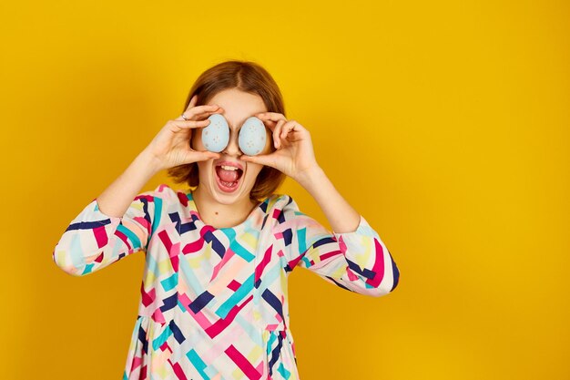 Heureuse adolescente ludique tenant des oeufs de Pâques peints couvrant les yeux