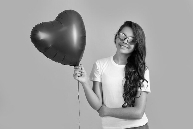 Heureuse adolescente à lunettes de soleil tenir un ballon de fête coeur rouge pour la fête romantique de symbole d'amour de la saint-valentin