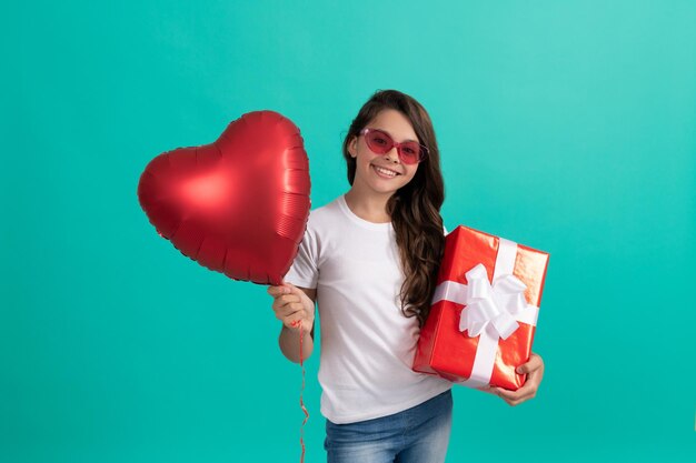 Heureuse adolescente à lunettes de soleil tenir la boîte-cadeau et la saint-valentin partie coeur ballon vente flash