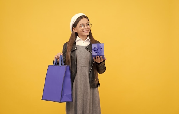 Heureuse adolescente de retour à l'école tenant une boîte-cadeau et un sac à provisions fond jaune copie espace présent