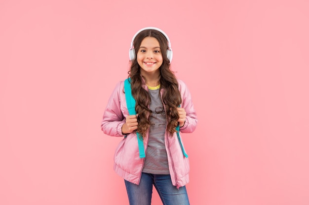 Heureuse adolescente avec sac à dos portant des écouteurs sur fond rose, école