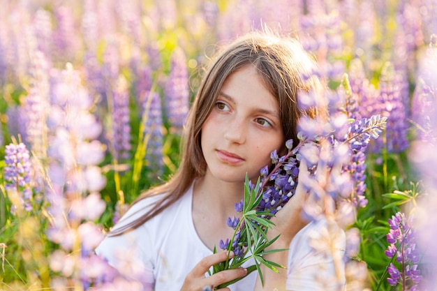 Heureuse adolescente souriante en plein air. Belle jeune femme de l'adolescence reposant sur le champ d'été avec fond vert de fleurs sauvages en fleurs