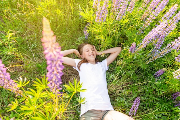 Heureuse adolescente souriante en plein air. Belle jeune femme adolescente reposant allongée sur le champ d'été avec fond vert de fleurs sauvages en fleurs. Enfant heureux gratuit se détendre et profiter de la nature.