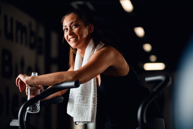 Heureuse athlète féminine ayant une pause dans l'eau en faisant du vélo sur un vélo stationnaire dans une salle de sport