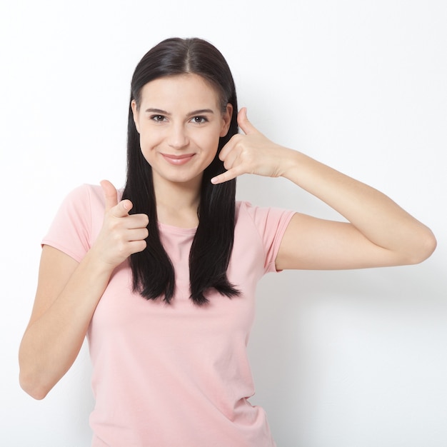 Heureuse belle brune aux cheveux longs en vêtements d'été fait un geste avec ses mains, appelez-moi