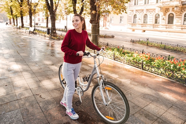 Heureuse belle dame vêtue d'un pull marchant avec son vélo dans la ville