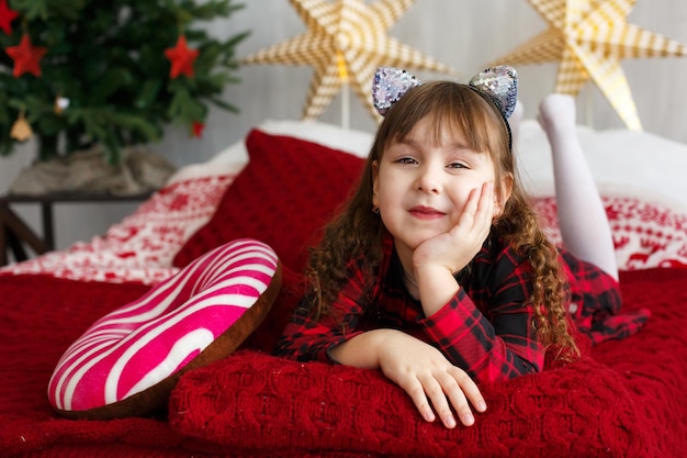 Heureuse belle enfant fille se trouve sur le lit avec arbre de Noël et décorations aux arrière-plans