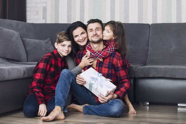 Heureuse belle famille donne un cadeau au père à l'occasion ensemble à la maison dans le salon