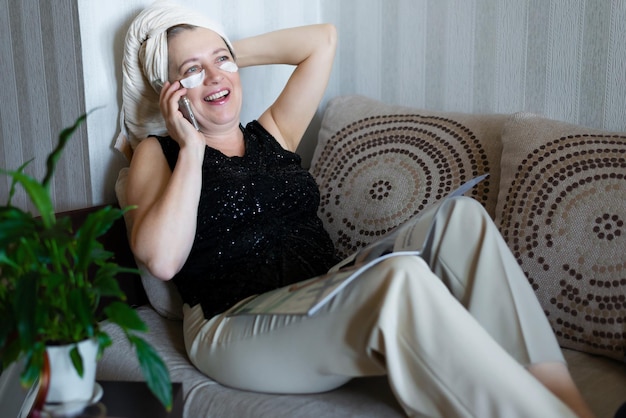 Heureuse belle femme d'âge moyen parlant au téléphone à la maison sur le canapé après une douche Concept de soins personnels Position de vie active des personnes âgées Technologies modernes