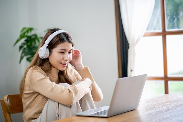 Heureuse belle femme asiatique portant des écouteurs à l'aide d'un ordinateur portable au travail ou en écoutant de la musique