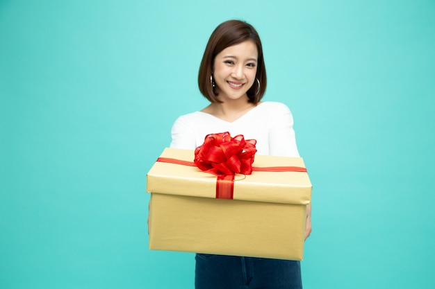 Heureuse belle femme asiatique sourire et tenant une boîte-cadeau isolée sur un mur blanc.