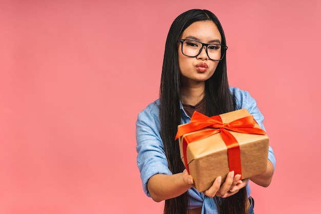 Heureuse belle femme asiatique tenant une boîte-cadeau isolée sur fond rose