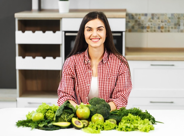 Heureuse et belle femme en chemise à carreaux décontractée et t-shirt blanc tourné à l'intérieur à la table de cuisine concept de consommation d'aliments sains