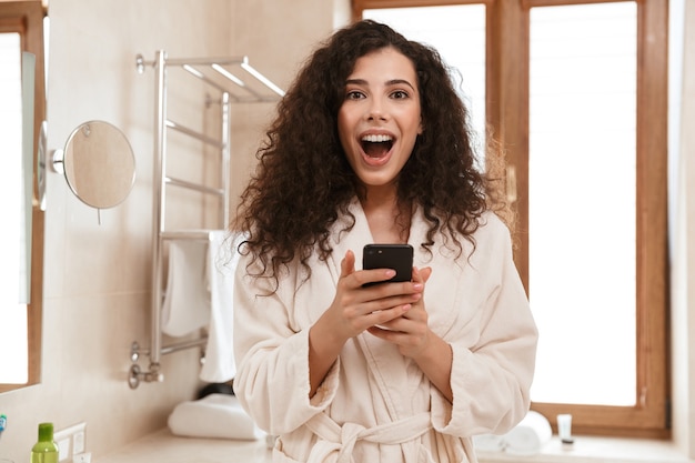 Heureuse belle femme dans la salle de bain à l'aide de téléphone mobile.