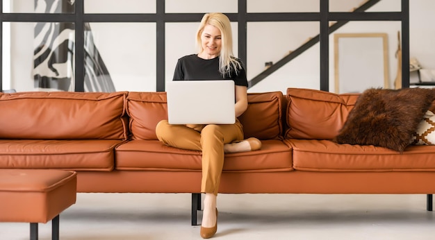 Heureuse belle femme décontractée travaillant sur un ordinateur portable assis dans la maison.