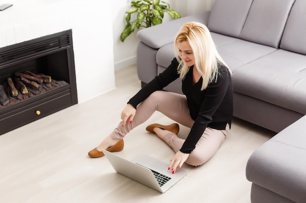 Heureuse belle femme décontractée travaillant sur un ordinateur portable assis par terre dans la maison.