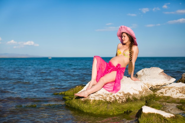 Heureuse belle femme enceinte en maillot de bain relaxant à la plage Le concept de santé et de repos
