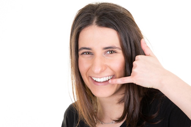 Heureuse belle femme en fond blanc souriant faisant un geste de téléphone avec la main et les doigts comme parler au téléphone portable