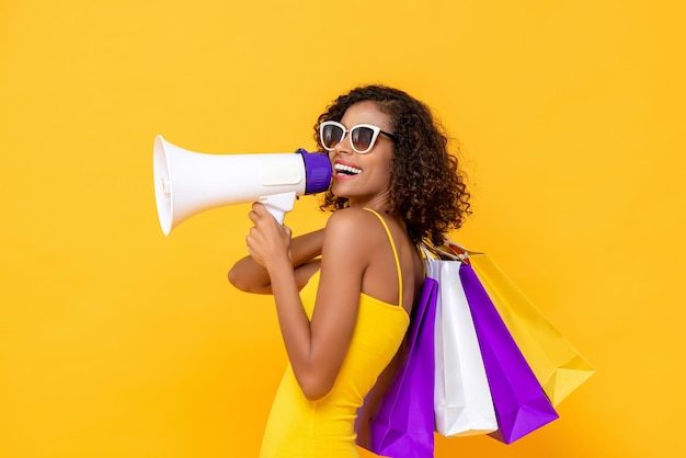 Heureuse belle femme avec des sacs à provisions et mégaphone sur fond jaune coloré isolé pour les concepts de vente et de remise