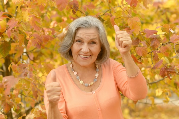 Heureuse belle femme senior dans le parc en automne avec les pouces vers le haut