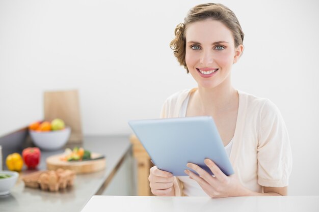 Heureuse belle femme tenant sa tablette assis dans sa cuisine à la maison