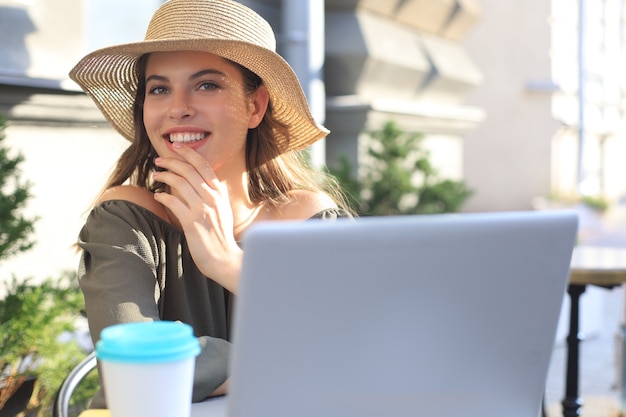 Heureuse belle femme travaillant sur ordinateur portable au café de la rue.