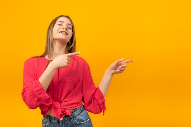 Heureuse belle fille adolescente souriante et pointant le doigt de côté isolé sur fond jaune Copier l'espace