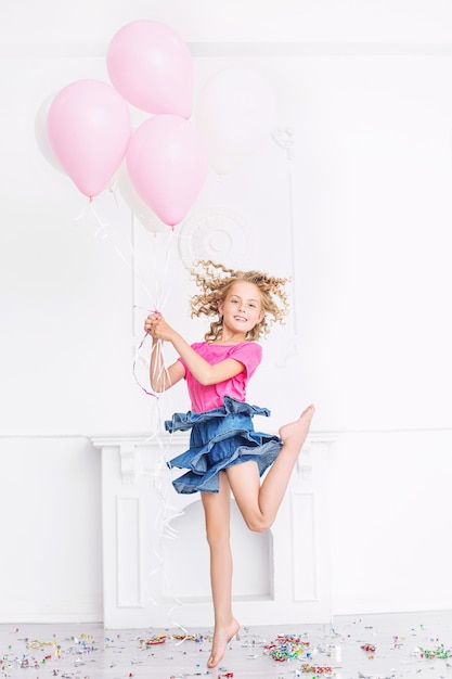 Heureuse belle fille mignonne d'enfant avec le sourire à la fête de vacances avec des ballons et des confettis dans la salle blanche