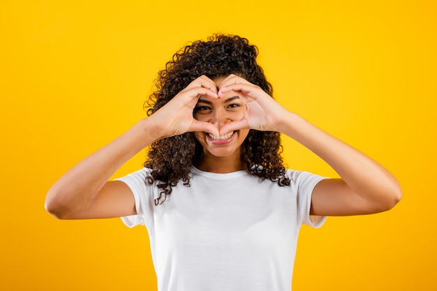 Heureuse belle fille noire montrant le coeur avec les mains isolées sur jaune