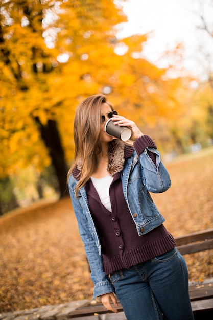 Heureuse belle jeune femme buvant du café en plein air au parc automne