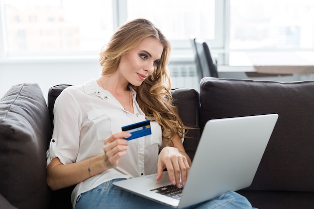 Heureuse belle jeune femme faisant des achats sur Internet à l'aide d'une carte de crédit à la maison