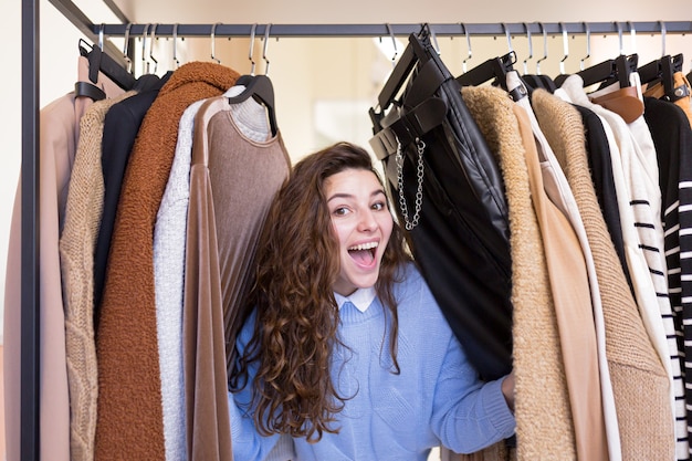 Heureuse belle jeune femme faisant du shopping dans un magasin de vêtements se réjouit du grand choix et des soldes